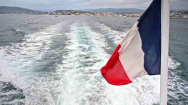 Fransız bayrağı yüzen bir teknede rüzgarda dalgalanıyor. Uzakta Cannes. Fransa. Yavaş çekim