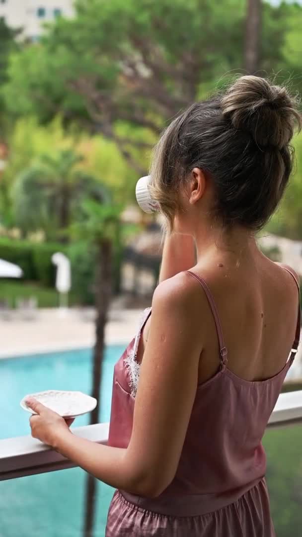 法国格拉西 一位身穿睡衣 身穿咖啡的女人站在酒店的阳台上 在绿油油的背景下摆着姿势 慢动作纵向观点 — 图库视频影像
