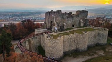 Romanya 'nın Targu Neamt kentindeki Neamt Kalesi' nin insansız hava aracı görüntüsü. Tepenin tepesindeki kale, çevresi yemyeşil ormanlarla, turistlerle, arka plandaki kasabalarla çevrili.