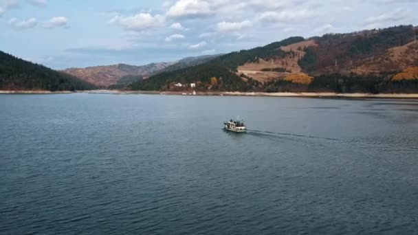 在罗马尼亚比卡兹湖上漂浮的一艘船的空中无人驾驶图片 覆盖着茂密森林的小山 — 图库视频影像