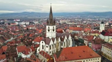 Romanya 'daki Sibiu Lutheran Katedrali' nin insansız hava aracı görüntüsü. Çıplak ağaçlar, birden fazla bina ve şehir manzarası olan bir sokak.