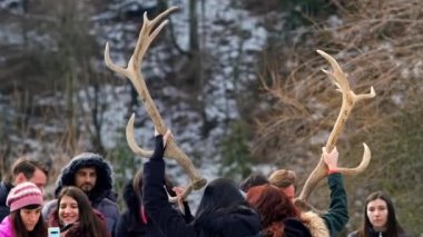 POIANA NEAMTULUI, ROMANIA - Aralık 2021: Kadınlar geyik boynuzu tutuyor, diğer insanlar Karpatlar 'da bir çimenlikte, etrafındaki ormanlarda