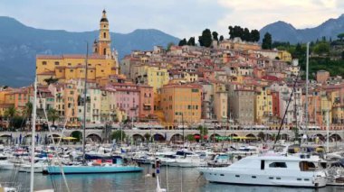 Menton, Fransa 'daki liman manzarası. Demirlemiş tekne ve yatlar, arka planda Aziz Michel Bazilikası, birden fazla bina.