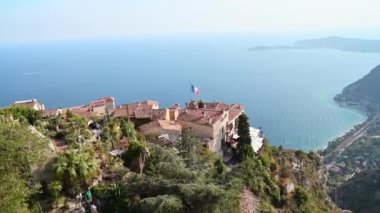Fransa, Menton 'da tropikal bitkilerle park et. İnsanlar, geleneksel konut binalarının çatıları, arka planda deniz.