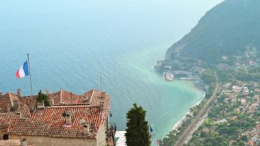 Menton, Fransa 'nın şehir manzarası. Ulusal bayrağı olan geleneksel yerleşim yerlerinin çatıları, arka planda deniz kıyıları.