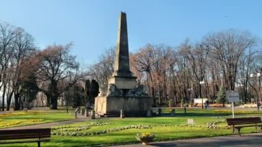 Romanya 'nın Iasi kentindeki Copou Park manzarası. Aslanlar Obelisk, sokaklar, çıplak ağaçlar, yeşil çimenler ve çiçek yatakları, insanlar
