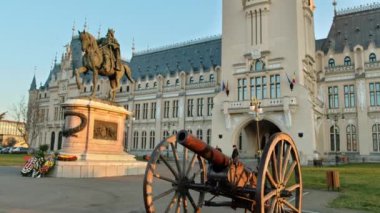 IASI, ROMANIA - 2021 ARALIK: Günbatımında şehir merkezindeki Kültür Sarayı manzarası. Büyük Stephen heykeli, eski top ve insanlarla dolu bir meydan.