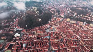 Romanya, Brasov 'un kışın hava aracı görüntüsü. Eski şehir merkezi, konut binaları, dağlar, alçak bulutlar ve sis havada