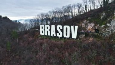 Kentin yakınındaki tepenin tepesinde Brasov tabelası, çıplak ağaçlar, turistler, alçak bulutlar, Romanya