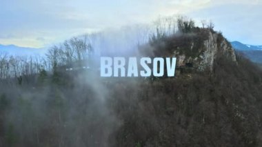 Kentin yakınındaki tepenin tepesinde Brasov tabelası, çıplak ağaçlar, turistler, alçak bulutlar, Romanya