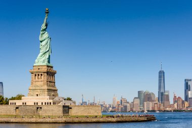 New York, ABD 'deki Özgürlük Anıtı manzarası. Adada çok sayıda turist, arka planda gökdelenler.