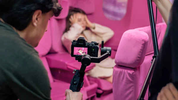 ピンクの飛行機の座席と壁を持つスタジオでポーズをとる若い女性の写真家 — ストック写真