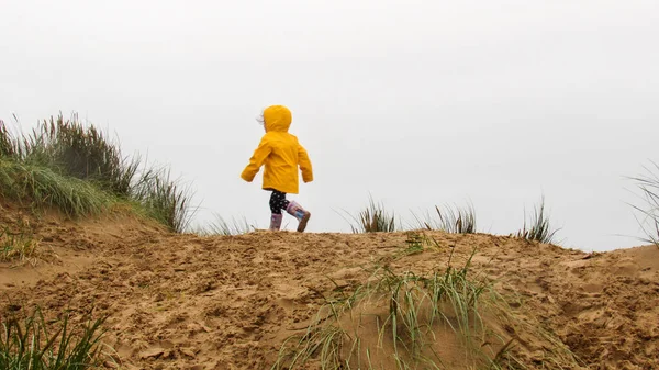 英国一个穿着雨衣的孩子在沙滩上的山上跑步 — 图库照片