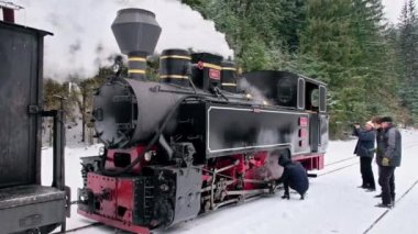 VISEU DE SUS, ROMANIA - HAZİRAN 2022 Kışın bir tren istasyonunda Mocanita buharlı treninin görüntüsü, kar, işçiler, çıplak orman
