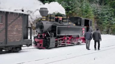VISEU DE SUS, ROMANIA - HAZİRAN 2022 Kışın bir tren istasyonunda Mocanita buharlı treninin görüntüsü, kar, işçiler, çıplak orman