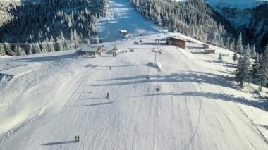 Romanya 'nın kışın Karpatlar' daki bir kayak pistinin insansız hava aracı görüntüsü. Kayak yapan insanlar, etrafta çıplak orman, kar, teleferik...