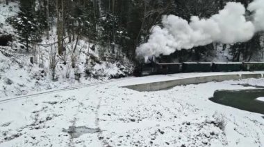 VISEU DE SUS, ROMANIA - HAZİRAN 2022 Kışın nehir boyunca bir vadideki Mocanita buharlı treninin hava aracı görüntüsü, çıplak orman ve karla kaplı tepeler