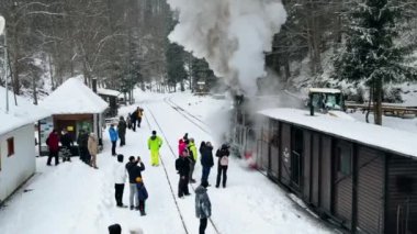 VISEU DE SUS, ROMANIA - HAZİRAN, 2022: Mocanita buharlı treninin kışın bir tren istasyonundaki hava aracı görüntüsü, kar, bir sürü yolcu, çıplak orman