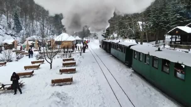 VISEU DE SUS, ROMANIA - JANUARY, 2022: Aerial drone view of the steam train Mocanita on a railway station in winter, snow, a lot of passengers, bare forest around