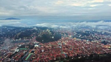 BRASOV, ROMANIA - 2021 ARALIK: Turistlerin bakış açısı ve kışın şehir manzarası. Eski şehir merkezi, konut binaları, alçak bulutlar ve sis havada