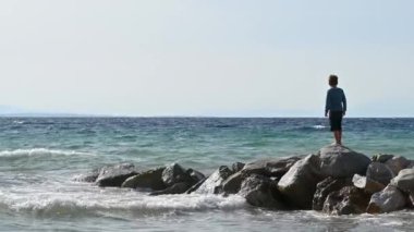 SALONIKI, GREECE - EPTEMBER, 2020: Yunanistan 'ın Selanik kentinde Ege kıyısı. Sahilde kayalıklarda oynayan çocuk.