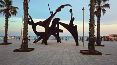 BARCELONA, İspanya - 10 Haziran 2021: Akdeniz kıyısındaki Embankment Caddesi, gün batımında. Birden fazla insan, otel, sanat kurulumu ve avuç içi