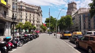 BARCELONA, İSPAN-HAZİRAN 2021: Yürüyen insanlar, güneşli bir günde klasik tarzda yapılmış eski binalar, yeşillikler, arabalar.