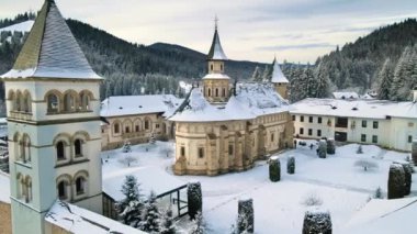 Romanya 'daki Putna Manastırı' nın kışın insansız hava aracı görüntüsü. Yürüyen turistlerle, çıplak ağaçlarla, karla, tepelerle dolu bir bahçe.