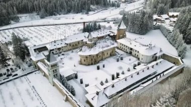 Romanya 'daki Putna Manastırı' nın kışın insansız hava aracı görüntüsü. İç avlu, çıplak ağaçlar, kar, tepeler, vadi