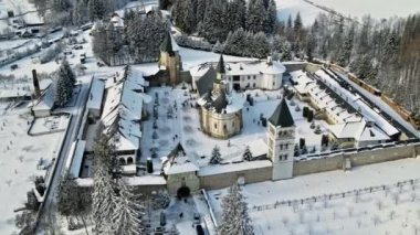 Romanya 'daki Putna Manastırı' nın kışın insansız hava aracı görüntüsü. Yürüyen turistlerle, çıplak ağaçlarla, karla, tepelerle dolu bir bahçe.