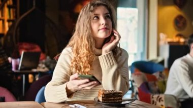 Kafedeki kahveciye Uluslararası Aşı Sertifikası COVID-19 ile akıllı telefon gösteren bir kadın. Arttırıcı doz. QR kodunu tarıyorum. Kafenin içinde, içinde pasta olan bir masa.