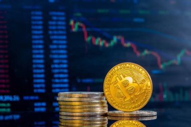 Koyu bir yansıtıcı yüzeyde altın Bitcoinlerin yakın plan çekimi ve arka planda azalan şifreleme histogramı