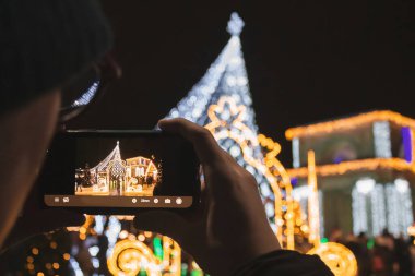 Genç adam süslü Noel ağacının fotoğrafını çekiyor. Arka planda Zafer Kemeri.