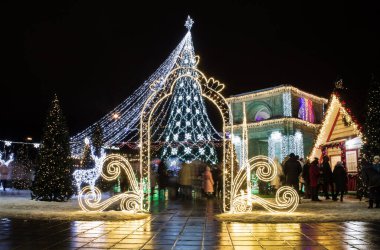 Şehrin merkezinde şenlikli doratif ışıklar ve Noel ağacı. Etrafta dolaşan insanlar. Zaman Çizelgesi.