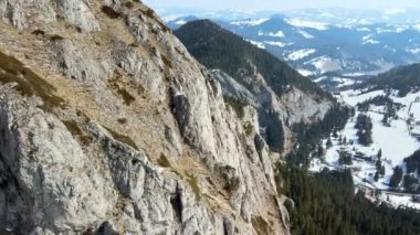 Romanya 'daki Karpatlar' ın insansız hava aracı görüntüsü. Kayalık yamaçlar ve köylü vadi, kısmen karla kaplı orman.