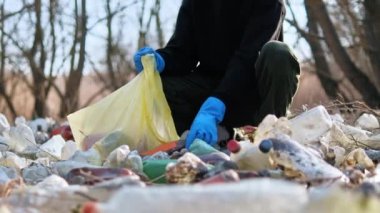 Adam doğada yerden plastik şişeler topluyor.