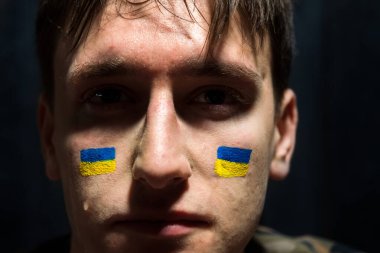 Yanaklarında Ukrayna 'nın ulusal bayrakları ve trajik bakışları olan ağlayan bir adam.