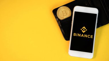CHISINAU, MOLDOVA - Mart 2022: Fiziksel Bitcoin altın madeni para, Binance uygulaması bir telefon, cüzdan, sarı arka plan
