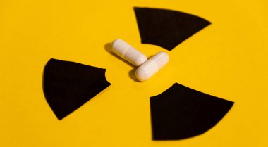 Two anti-radiation pills based on pottasium iodine on a yellow background and the radiation warning sign clipart