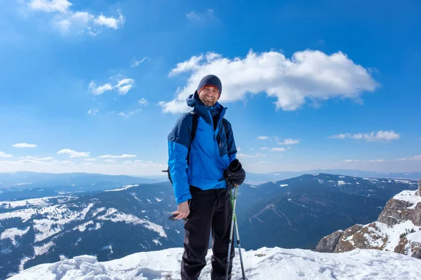 BICAZ, ROMANIA - 2022 MART: Mavi ceketli bir yürüyüşçü karlı dağların manzarasının ön planında kameraya gülümsüyor