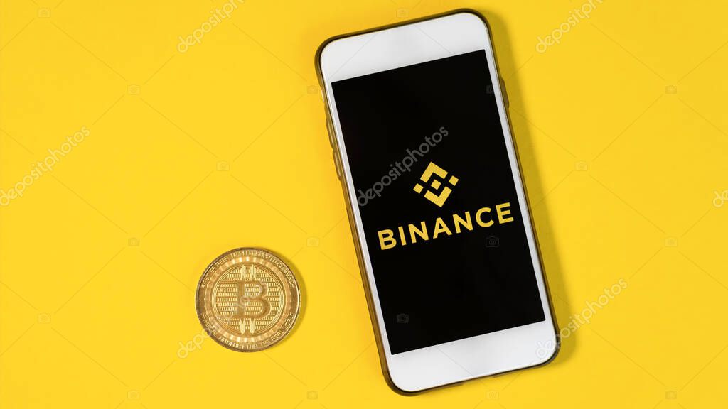 CHISINAU, MOLDOVA - MARCH, 2022: Physical Bitcoin gold coin, Binance app opened on a phone, yellow background