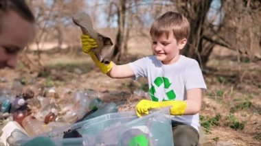 Erkek ve kız, kirlenmiş bir temizleme kabında plastik çöp topluyor tişörtlerdeki geri dönüşüm tabelalarını topluyor. Yavaş çekim