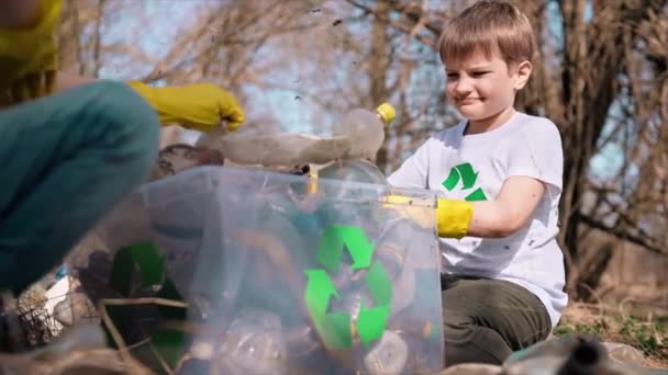 男孩和女孩在一个被污染的清洁容器中收集塑料垃圾 回收T恤衫上的标识 慢动作 — 图库视频影像