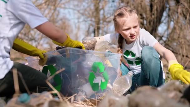 男孩和女孩在一个被污染的清洁容器中收集塑料垃圾 回收T恤衫上的标识 慢动作 — 图库视频影像