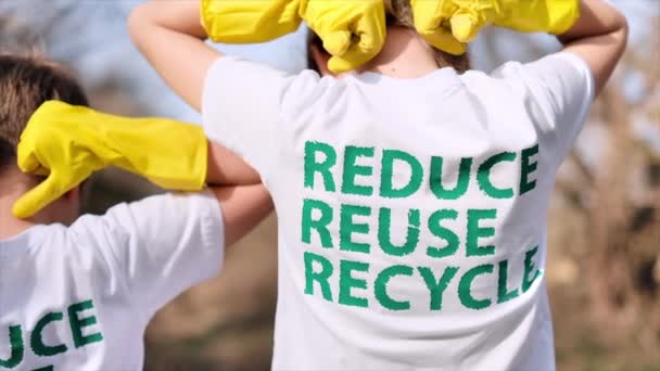 戴着橡胶手套的男孩和女孩在他们T恤衫上的生态题词上展示 在受污染的地方收集塑料垃圾 — 图库视频影像