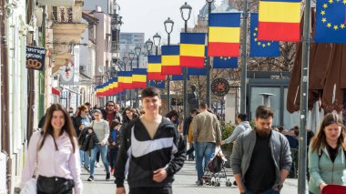 CLUJ, ROMANIA - Nisan 2022: Şehir merkezinin sokak manzarası. Yürüyen bir sürü insan, bayraklar, eski binalarla dolu bir yaya sokağı.