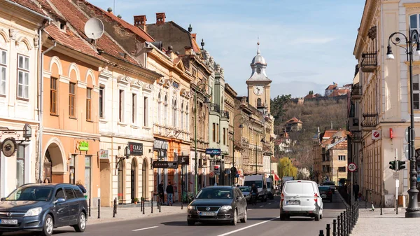 BRASOV, ROMANIA - Nisan 2022: Eski şehir merkezi manzarası. Eski binalar, yürüyen insanlar, arabalar.