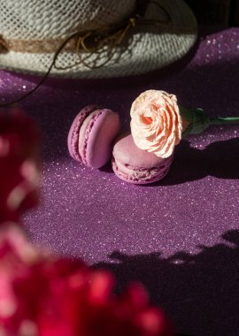 İki mor badem kurabiyesi ve çiçek arkaplanında bir gül, parlak mor arka plan.