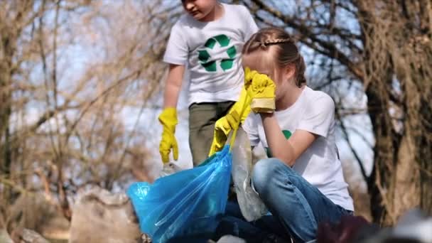 Мальчик Девочка Собирают Пластиковый Мусор Мешок Загрязненной Поляне Вывески Футболках — стоковое видео