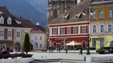 BRASOV, ROMANIA - Nisan 2022: Eski şehir merkezindeki Konsey Meydanı manzarası. Klasik binalar, yürüyen ve dinlenen bir sürü insan, Siyah Kilise.